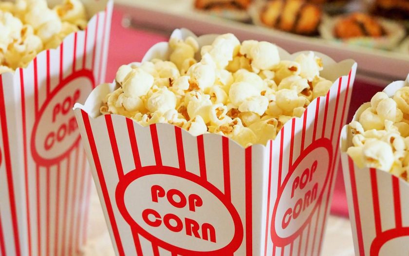 Une image alléchante de pop-corn beurré débordant d'un récipient classique à rayures rouges et blanches, prêt à être dégusté lors d'une soirée cinéma.